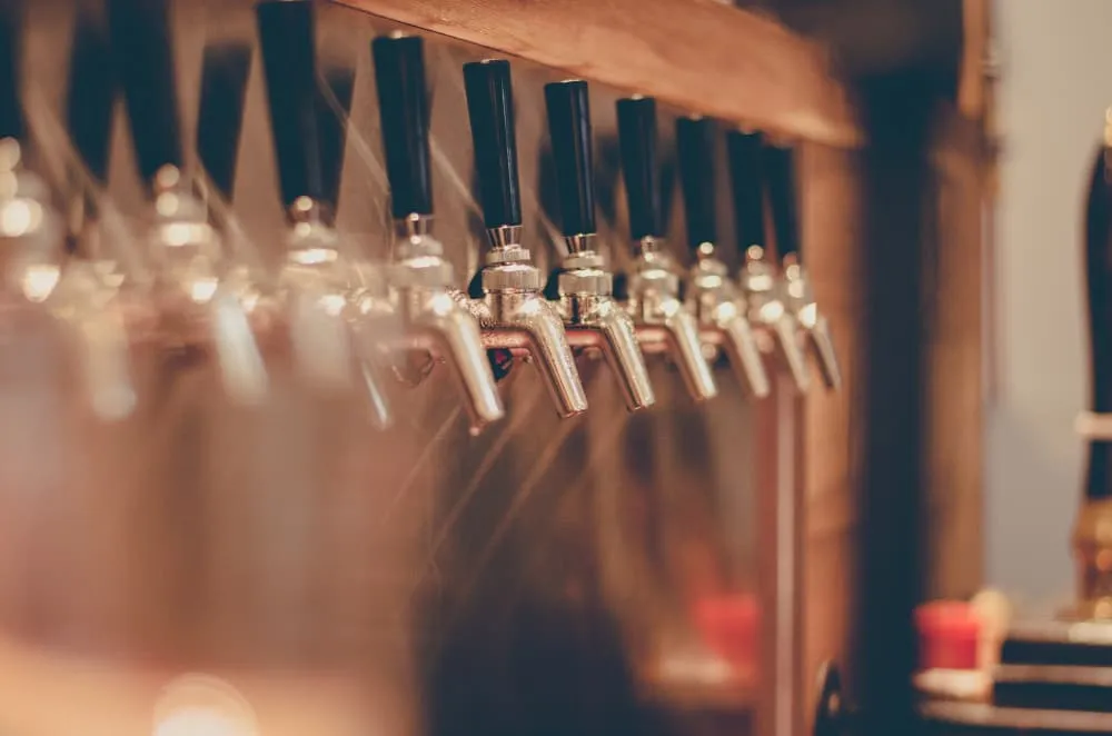 Row of metal beer taps with black handles in a bar setting.