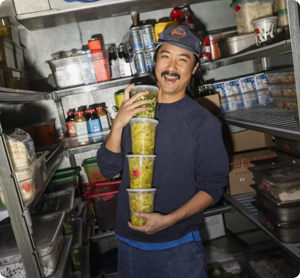 Restaurant owner smiling in walk-in cooler holding stacked food prep containers