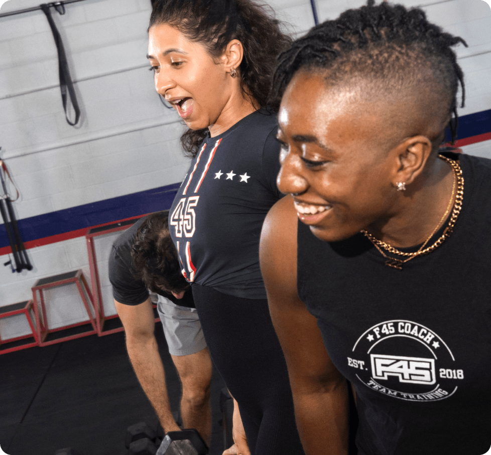 an f45 coach smiling alongside gym members during a workout session in a fitness studio. this highlights the app's capability to support multi-location scheduling and team management for fitness franchises.