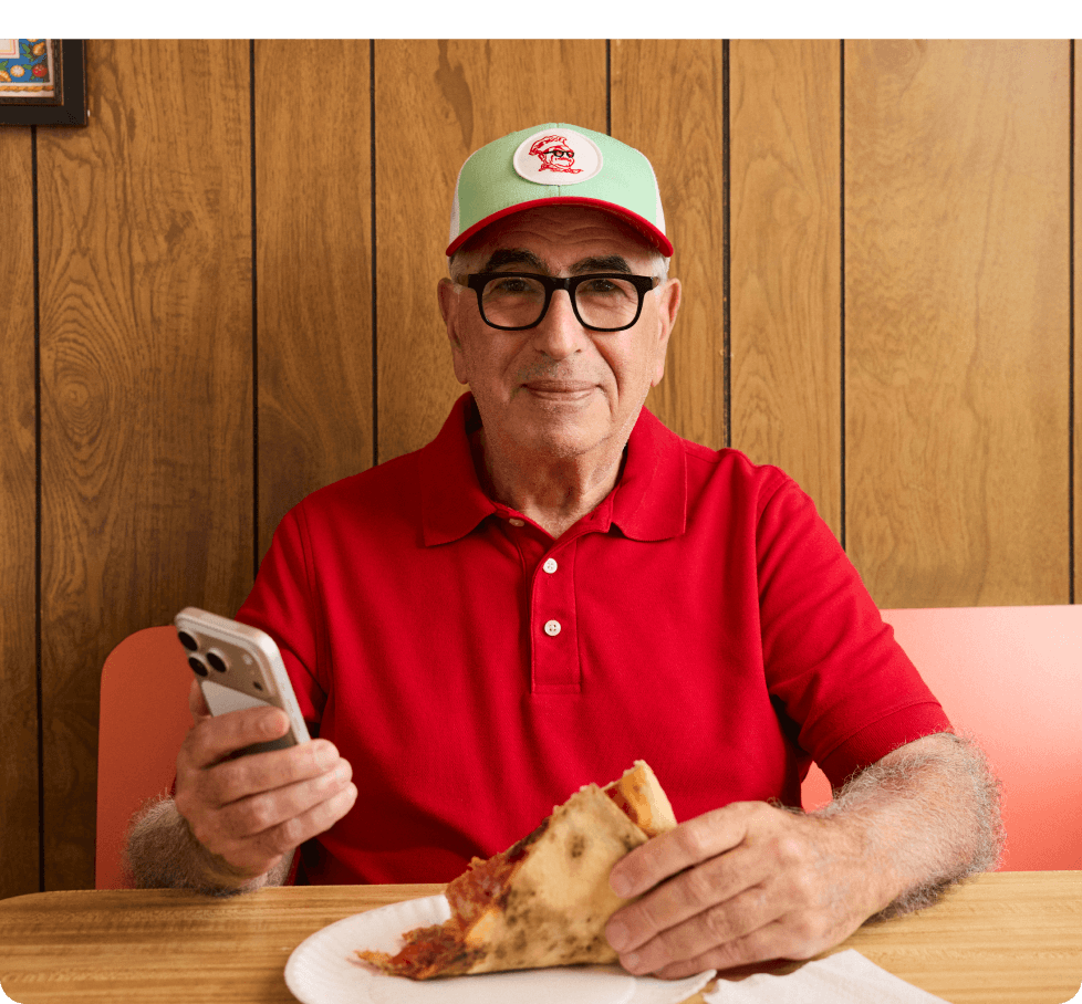 Homebase customer at his restaurant checking the homebase app while eating pizza.