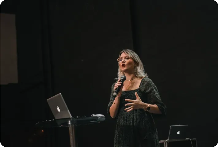 Speaker addressing an audience from a darkened stage beside an open laptop.