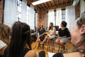 Small group seated in a circle in a brick-walled office during a team discussion.