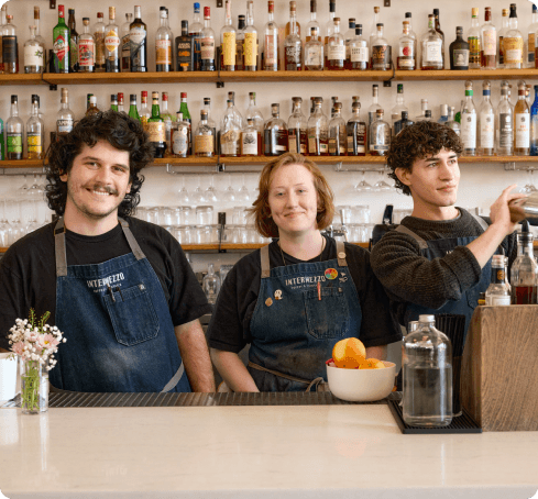 Three restaurant employees standing behind a bar smiling.