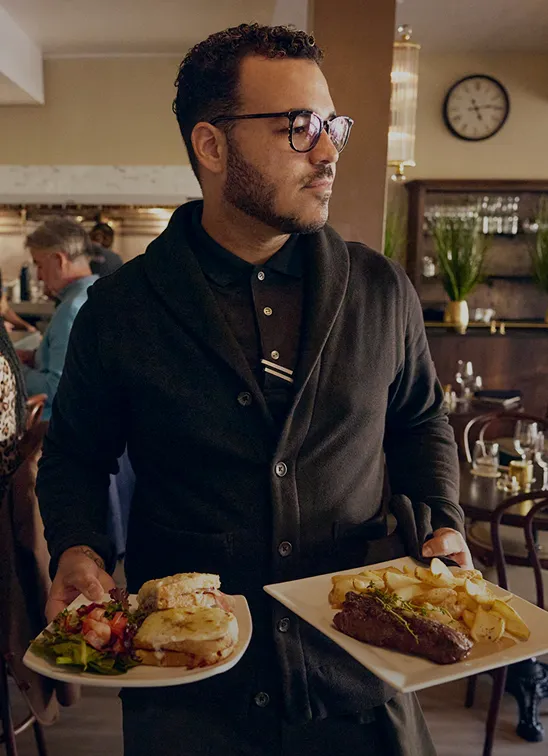 A restaurant server smiling while carrying two plates of food
