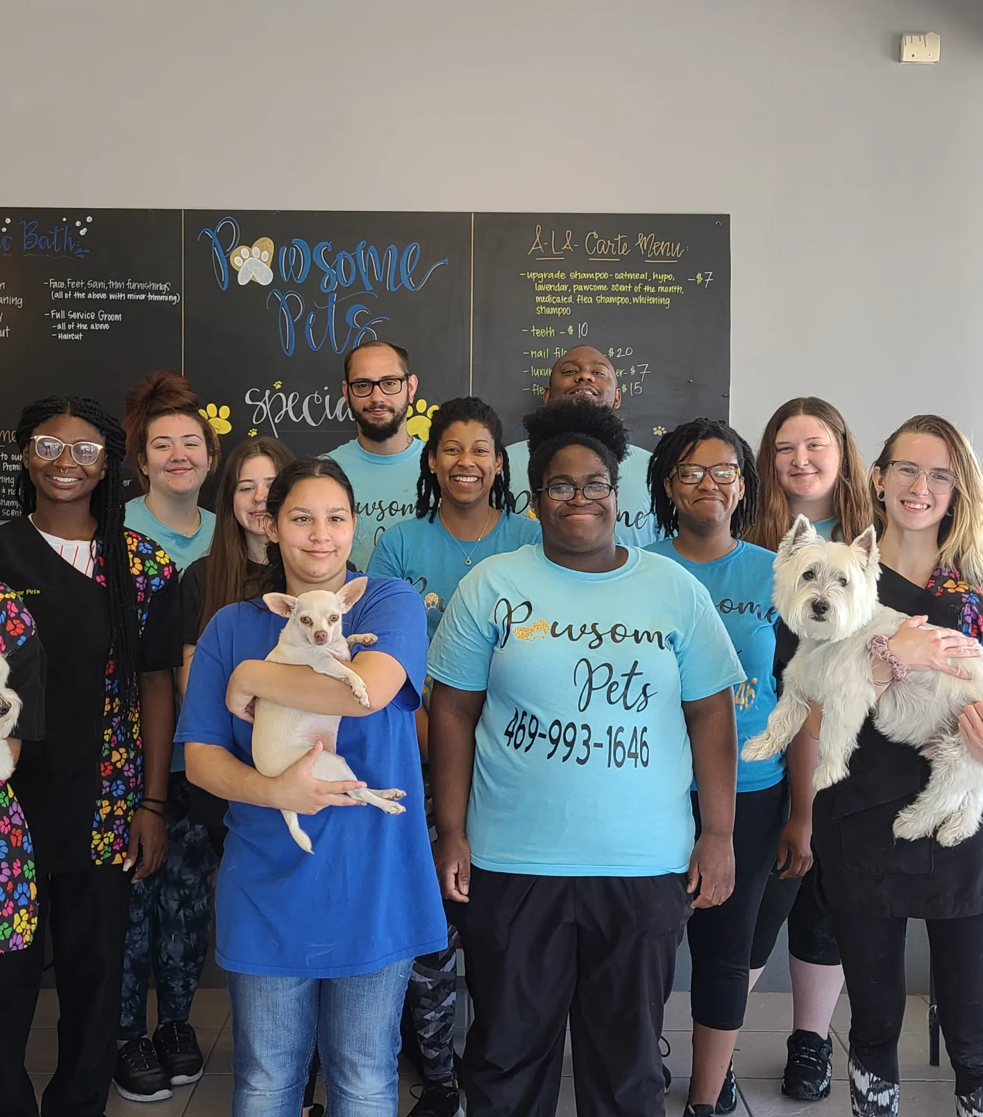 A pet care team posing indoors with two small dogs